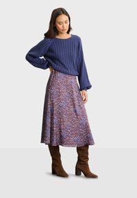 Blå randig tröja kombinerad med en mönstrad, flödande midikjol i bruna, blå och röda nyanser, bärs med bruna knähöga blockhälsskor.