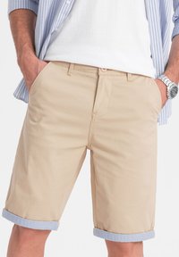 Shorts in cotone beige con tasche frontali, orli arrotolati con interno azzurro chiaro e chiusura con bottone standard in vita.