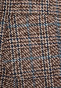 Brązowa i beżowa tkana tkanina z wzorem w kratę, z niebieskimi i ciemnogranatowymi akcentami. Teksturowana, o ciasnym splocie i zróżnicowanej kolorystyce nici.
