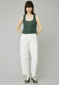 Un crop top vert sans manches avec des boutons à l'avant, un jean taille haute blanc et des baskets vert foncé avec des accents roses. Fond neutre.