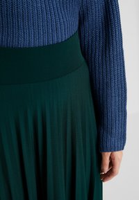 Stickad blå tröja med ribbad textur som matchas med en grön plisserad kjol med en slät midja och eleganta vertikala linjer.