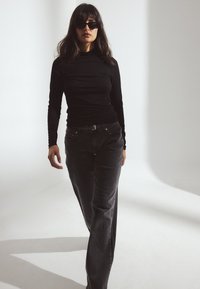 Zwarte lange mouwen top in combinatie met donkergrijze wijd-uitlopende jeans. Zonnebril voegt een moderne touch toe. Zachte stoffen, aansluitende stijl, minimalistisch ontwerp.