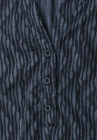 Gros plan d'une chemise gris foncé avec des rayures verticales noires irrégulières et trois boutons noirs au centre.