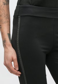 Leggings neri con vita alta, realizzati in un tessuto liscio ed elastico. Presentano un motivo grigio sottile lungo la cucitura laterale.