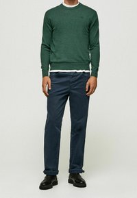 Groene gebreide trui met ronde hals, gecombineerd met donkerblauwe broek met opgerolde manchetten en zwarte enkellaarzen. Eenvoudig design, zachte textuur en slim-fit snit.
