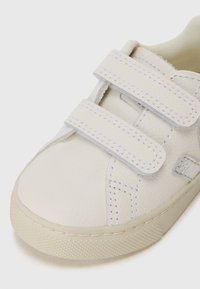 Hvite lær sneakers med to borrelåser, teksturert overflate, rund tå og kontrastsying. Lavprofil gummisåle.