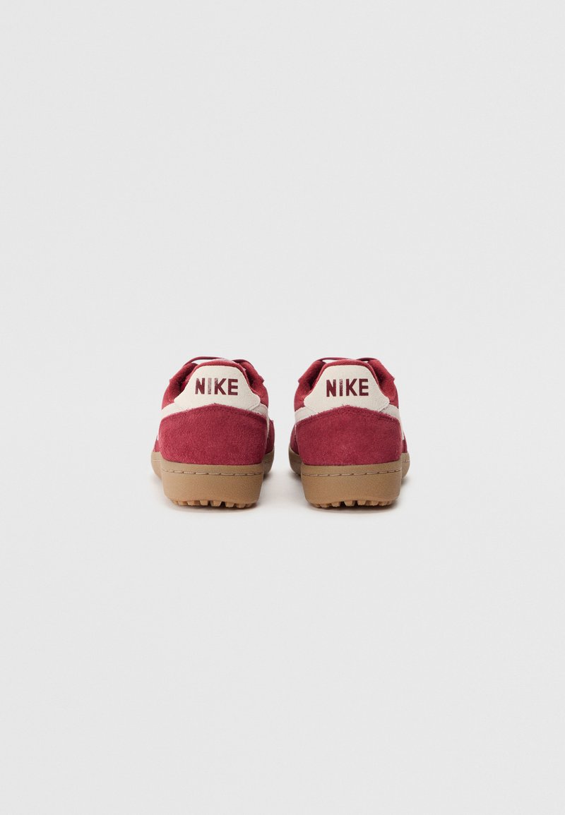 Baskets en suède rouge avec une semelle en caoutchouc marron, dotées d'accents blancs et du logo "NIKE" sur le talon. Design arrondi et surface texturée.