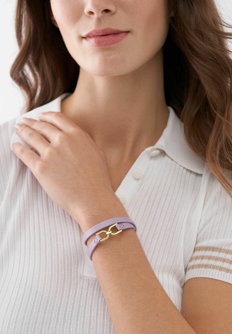 Purple leather bracelet with a gold clasp, featuring a double band design and a smooth texture. Worn on a wrist with a white polo shirt.