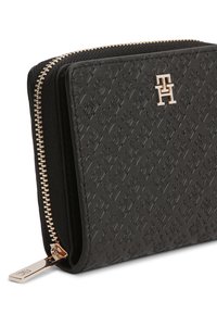 Μαύρο πορτοφόλι από δέρμα με ανάγλυφο σχέδιο, χρυσά μεταλλικά στοιχεία και κλείσιμο με φερμουάρ. Διαθέτει διακριτικό λογότυπο στο μπροστινό μέρος.