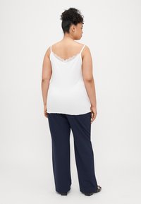 Camisola branca com renda no decote, combinada com calças largas de um azul marinho escuro, apresentando um tecido suave e um corte relaxado.