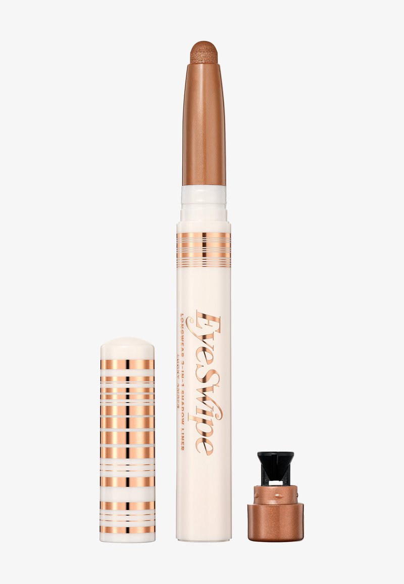 Kremowy cień do powiek w formie sztyftu z brązową nakrętką, ozdobiony złotymi i białymi paskami. Aplikator jest smukły i cylindryczny.