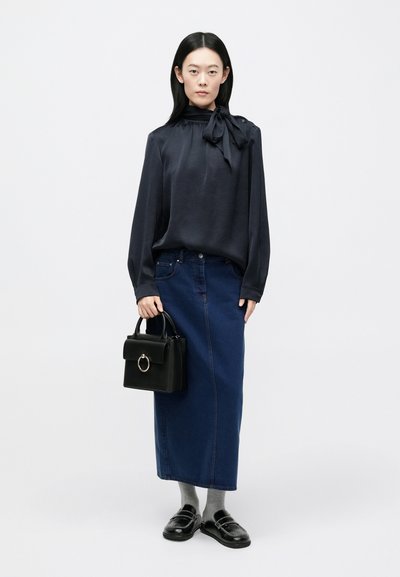 Blusa in raso blu navy con dettaglio a fiocco, abbinata a una gonna di jeans blu scuro. Borsa nera con manico circolare, calzini grigi e mocassini neri.