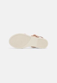 Semelle plate d'une sandale, présentant une semelle extérieure en caoutchouc texturé beige clair et une tige rose clair brillante avec un détail en boucle.