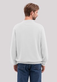 White sweatshirt with a relaxed fit, dropped shoulders, ribbed cuffs, and a rounded neckline, paired with dark blue jeans featuring distinctive pockets.