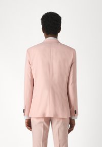 Giacca rosa chiaro con taglio sartoriale, apertura singola e dettagli con bottoni. La texture liscia e i rever affilati definiscono il design.