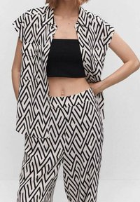 Ensemble en noir et blanc comprenant une chemise à manches courtes et un pantalon taille haute, fabriqué dans un tissu léger avec un design géométrique.