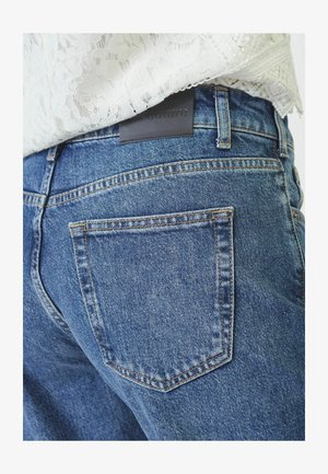 Jeans de mezclilla azul con un diseño clásico de cinco bolsillos y una etiqueta de cuero en la parte trasera. La tela tiene una textura desgastada con detalles de costura visibles.