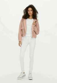 Light pink cropped jacket with elastic cuffs, worn over a white t-shirt and paired with white skinny jeans and white sneakers.