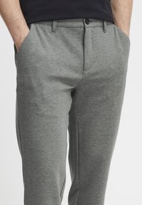Pantalones de punto grises con una textura suave, cinturilla estándar, bolsillos laterales y un diseño de pierna ajustada. Presenta un cierre con un solo botón negro.