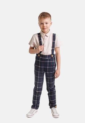 Granatowe spodnie na szelkach w kratę z czerwonymi i białymi akcentami, połączone z jasną koszulą i białymi trampkami. Regulowany pas na guziki.
