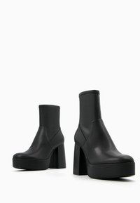 Černé kožené kotníkové boty s tlustou platformou a vysokým čtvercovým podpatkem. Elegantní design zahrnuje elastické boční panely a hladký povrch.