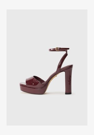 Sandal alta con tacco in pelle verniciata bordeaux, dotata di platform, cinturino alla caviglia e accentato da una fibbia dorata. Design elegante e finitura lucida.