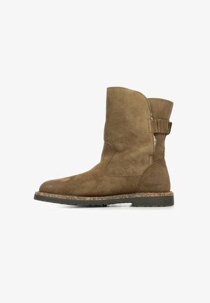 Bottine en daim marron avec un bout arrondi, un panneau latéral et une accentuation de sangle à l'arrière. Semelle texturée pour une meilleure adhérence.