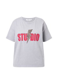 Camiseta de algodón gris claro de manga corta, que presenta un gráfico audaz en rosa con la palabra "STUDIO" y un diseño de rayo con estampado de leopardo.