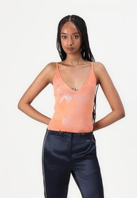 Orange ribbed tank top with a deep V-neck and fine shimmer design, paired with navy satin pants featuring side stripes and hardware accents.