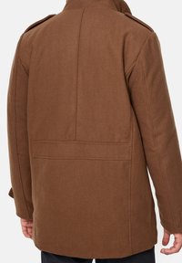 Bruine jas van een wolmix met een kraag, zichtbare naden en een strakke, rechte snit. Voorzien van een rugsplit en twee zijzakken.