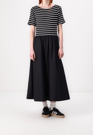 Robe maxi noire avec un corsage à manches courtes rayé et une taille froncée. Associée à des baskets noires et des chaussettes blanches courtes.