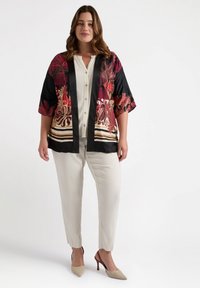 Seide Kimono-Jacke mit floralen Mustern in Rot, Gold und Schwarz, mit satinierter Oberfläche und offenem Vorderteil. Kombiniert mit einer cremefarbenen Bluse und Hose.