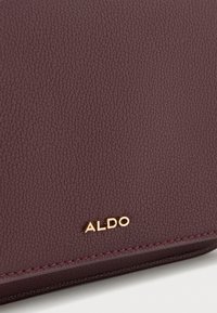 Portafoglio in ecopelle burgundy con texture, dettagli cuciti e logo "ALDO" dorato nell'angolo in basso a destra.