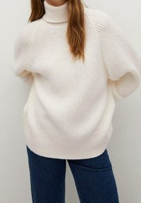 Gruby golf w miękkim, białym dzianinowym materiale, o luźnym kroju i prążkowanej fakturze, zestawiony z ciemnoniebieskimi dżinsami.