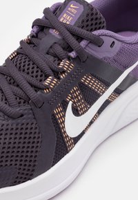 Fialovo-černá běžecká obuv Nike s horní částí z prodyšné síťoviny, texturovanými detaily, bílým logem Swoosh a kontrastními oranžovými akcenty. Lehký design.