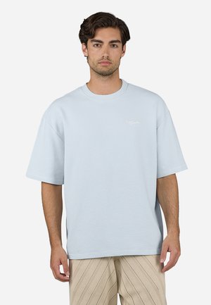 Ljusblå oversized t-shirt i våffeltextur med rund halsringning och korta ärmar, med en liten vit logotyp på bröstet.