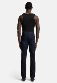 Jeans in denim blu scuro con una vestibilità dritta, dotati di tasche posteriori e dettagli di cucitura blu sottili, abbinati a una canotta nera.