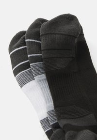 Three pairs of folded athletic ankle socks in black, gray, and white with striped patterns, stacked on a white background.
