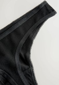 Schwarze Stringunterwäsche aus weichem Stoff, mit Spitzenbesatz an den Rändern und einer glatten Textur, die ein minimalistisches Design hervorhebt.