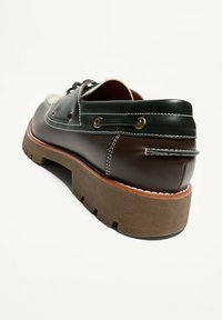 Férfi bőrcsónakcipő barna talppal, fekete és sötétbarna felsőrésszel, fehér varrással és fűzőrészletekkel az oldalak mentén.