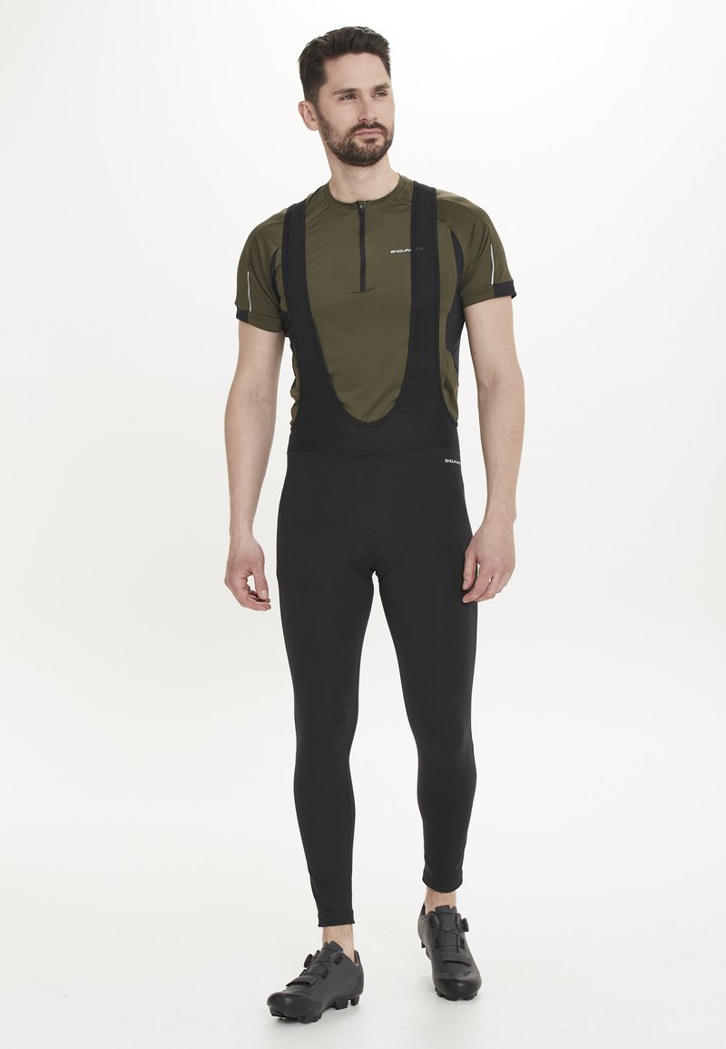 Cykeloutfit med en åtsittande svart bib och en olivgrön tröja med halv dragkedja. Innehåller ventilerande material, reflekterande detaljer och en kroppsnära design.