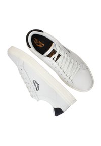 Baskets en cuir blanc avec une finition lisse, dotées de lacets ronds, d'une doublure noire douce et d'un logo prominent sur le côté.
