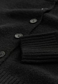 Czarny kardigan wykonany z teksturowanej wełny, z prążkowanymi mankietami i okrągłymi czarnymi guzikami, o lekko puszystej powierzchni.