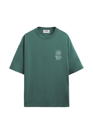Zelené oversize tričko s krátkým rukávem, bílým kruhovým logem a nápisem "Thank You" na levé straně hrudi, jednobarevné pozadí.