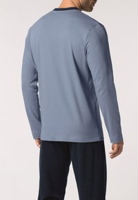 Camicia a maniche lunghe azzurro chiaro con colletto nero, morbido al tatto e orlo dritto, indossata con pantaloni scuri. La vista posteriore mette in mostra la vestibilità e il colore.