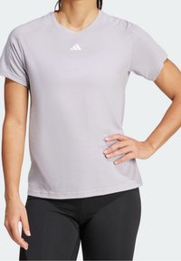 T-shirt de sport gris clair à manches courtes, fabriqué en tissu doux, avec un petit logo blanc près de l'encolure. Associé à un legging noir.