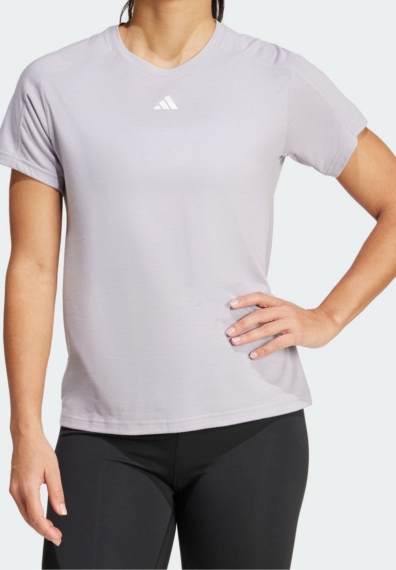 T-shirt de sport gris clair à manches courtes, fabriqué en tissu doux, avec un petit logo blanc près de l'encolure. Associé à un legging noir.