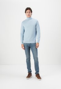 Suéter de cuello alto de punto color azul claro, combinado con jeans azul claro y zapatillas marrones. El suéter tiene un diseño ajustado y puños acanalados.