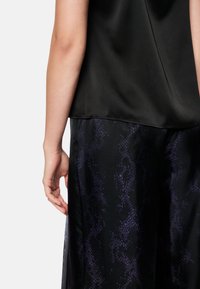 Black satin top with a smooth texture, paired with black pants featuring a purple snake print pattern. Visible hand gently touching the pants.