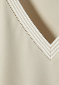 Top beige con escote en V y una tela texturizada. Las rayas horizontales blancas en el cuello enfatizan la forma y el diseño del escote.